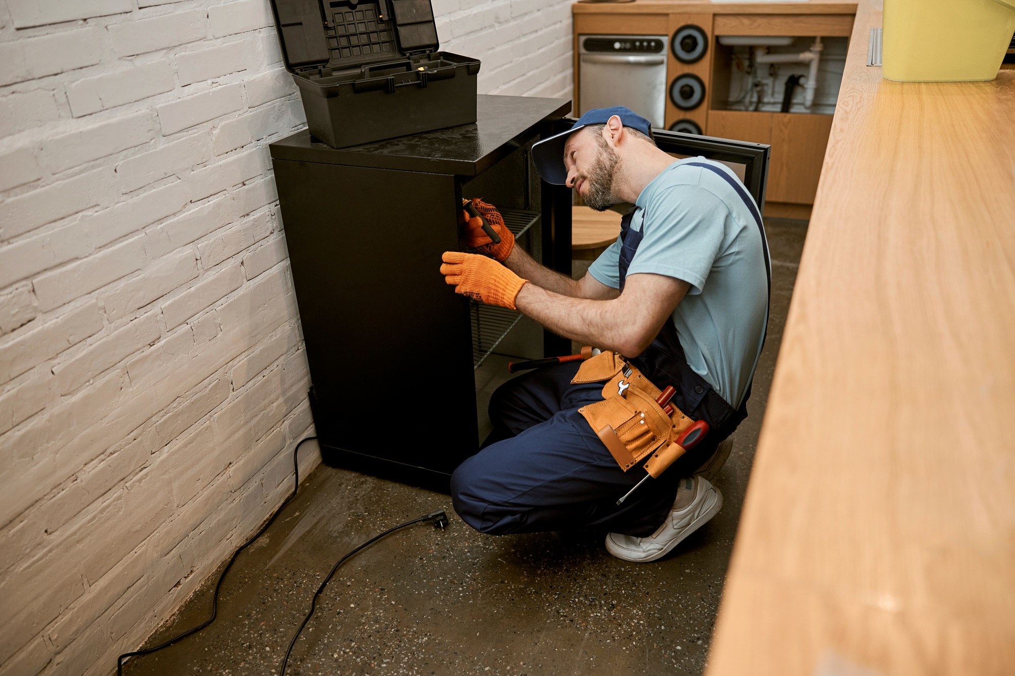 Bearded young man repairing fridge in kitchen