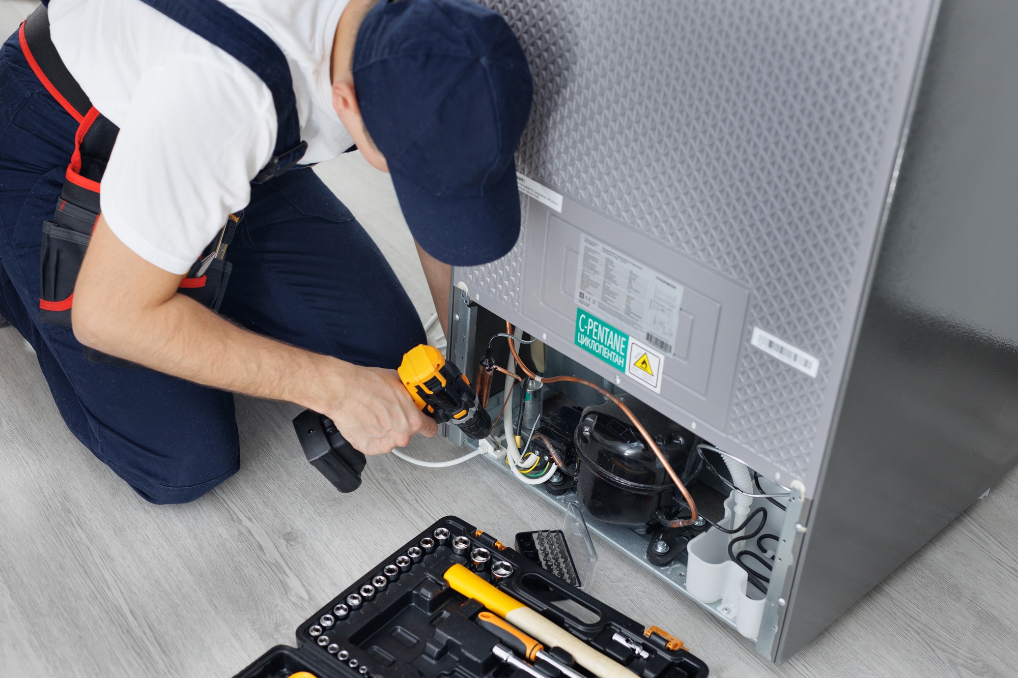 Male technician repairs a refrigerator in the kitchen in close-up.