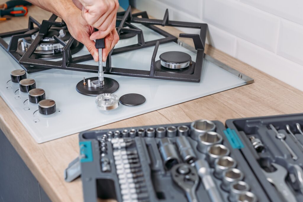 man's hand repairs hotplate of gas panel with screwdriver