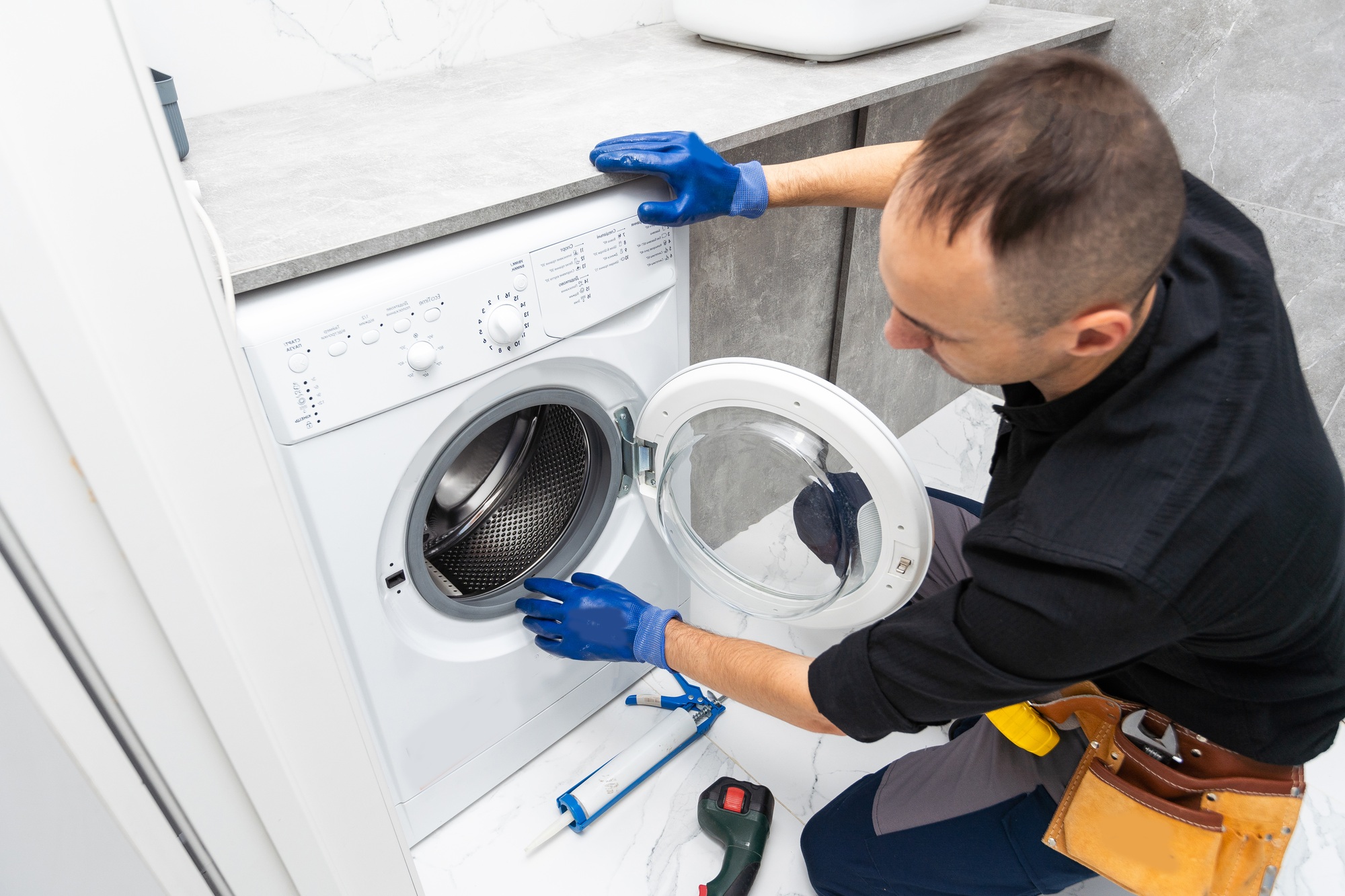 Plumber fixing washing machine on white background